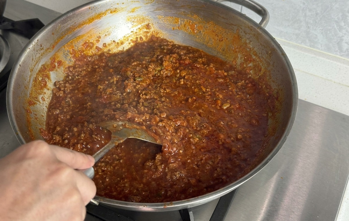 Mano usando una espátula de metal para integrar la mantequilla en la salsa espesa de color rojo oscuro.