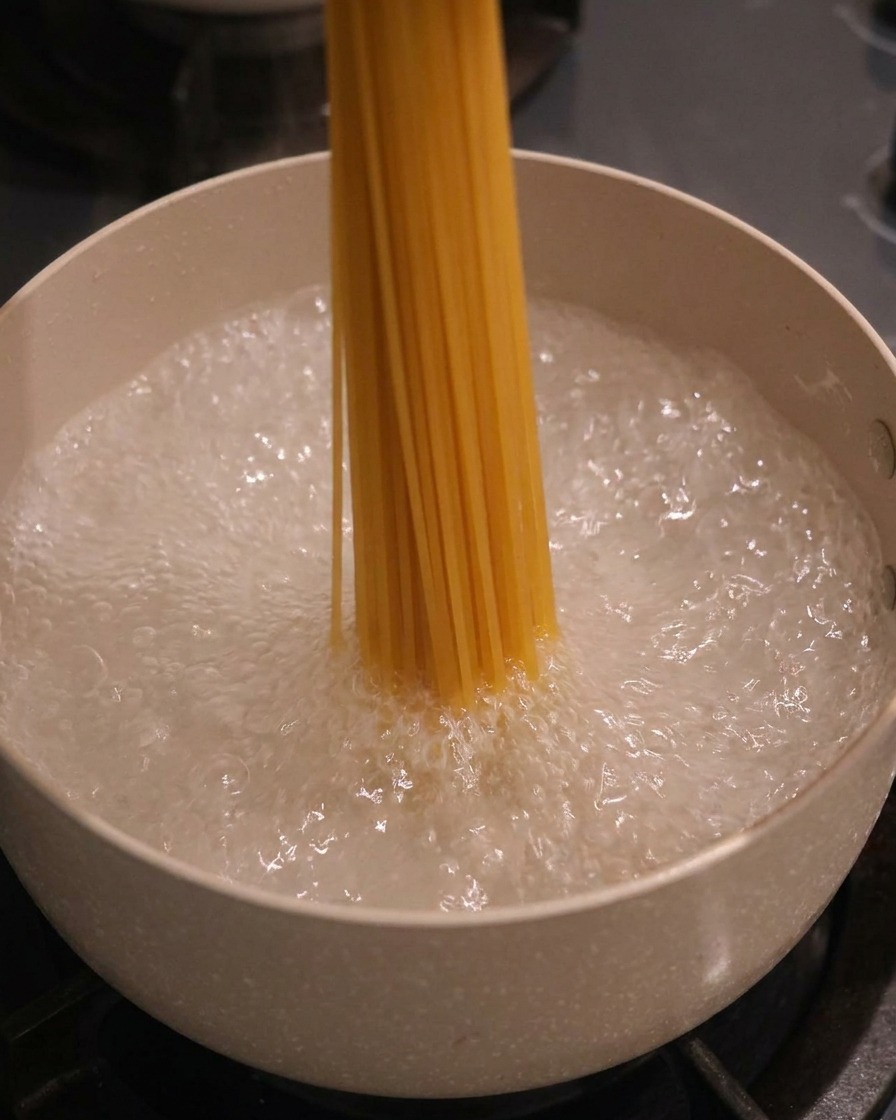 Un manojo de espaguetis secos introduciéndose verticalmente en una olla con agua hirviendo.