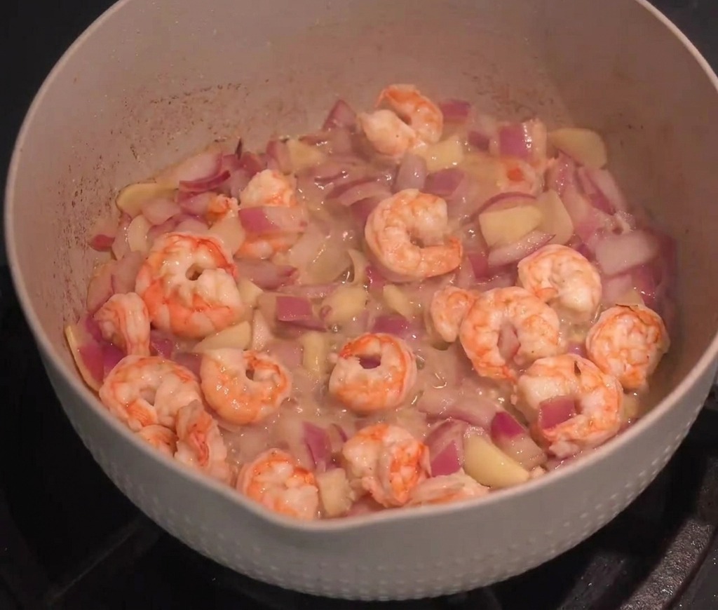 Camarones frescos salteados con cebolla y ajo en una sartén grande.