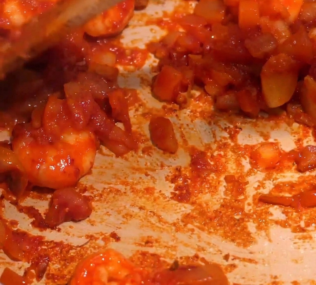 Una salsa roja espesa de camarones removiéndose en una sartén mientras se añade líquido para crear un hervor suave.