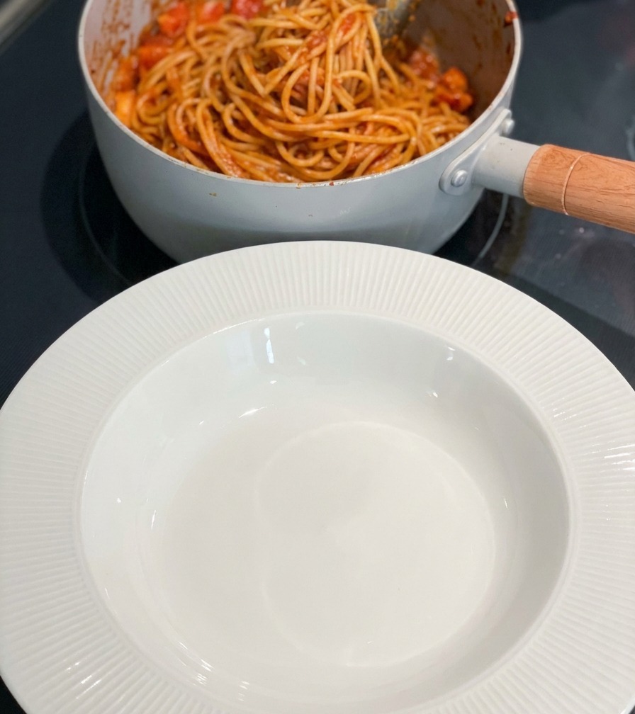 Una olla de pasta picante con camarones terminada junto a un bol blanco vacío sobre la encimera.