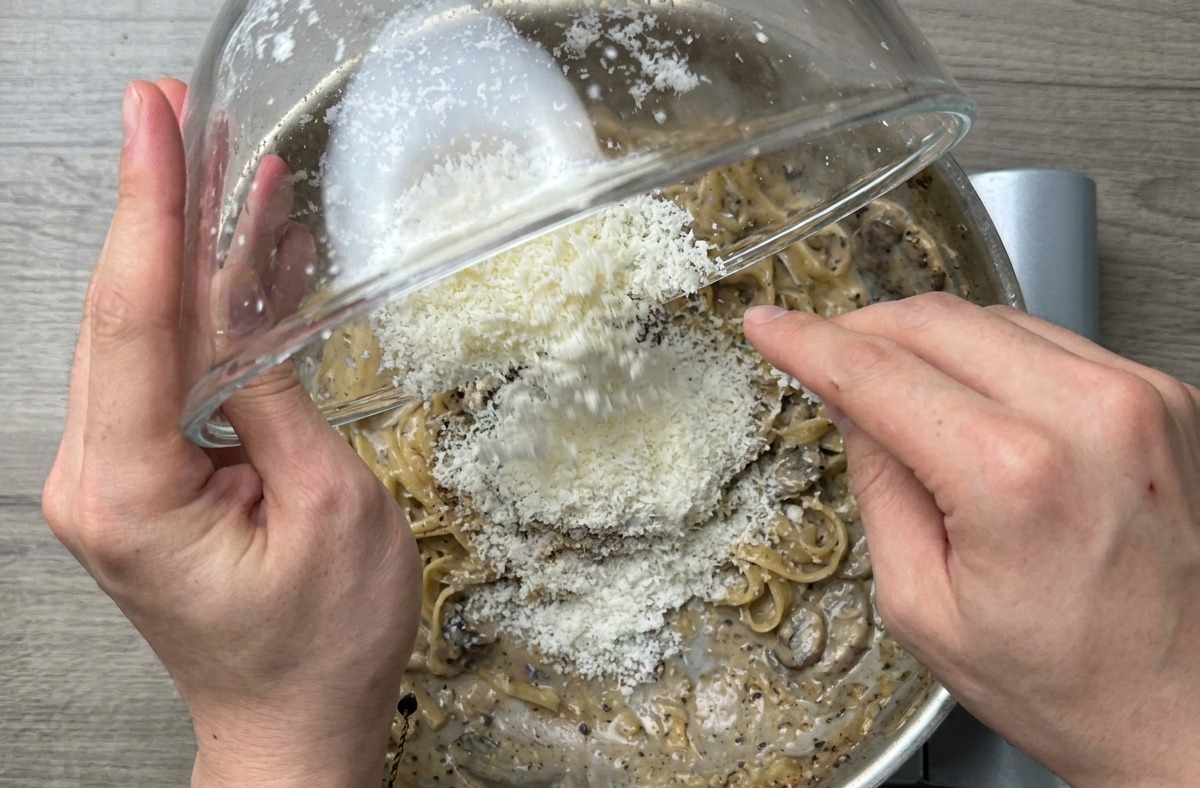 Primer plano de los espaguetis terminados siendo salteados vigorosamente en la sartén para lograr una salsa brillante.