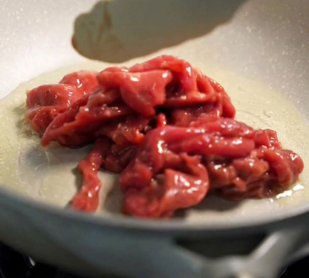 Unas pinzas colocando la carne cruda marinada en una sartén caliente con aceite.