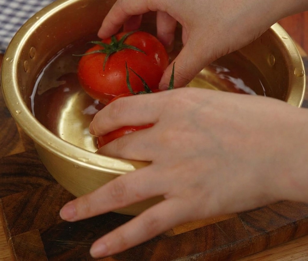 Dos tomates rojos congelados sumergidos en un bol metálico con agua.