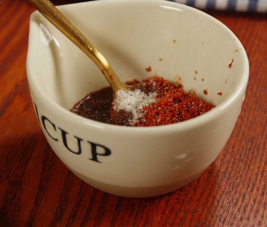 Mezclando una salsa roja con pasta de chile y especias en una pequeña taza de cerámica.