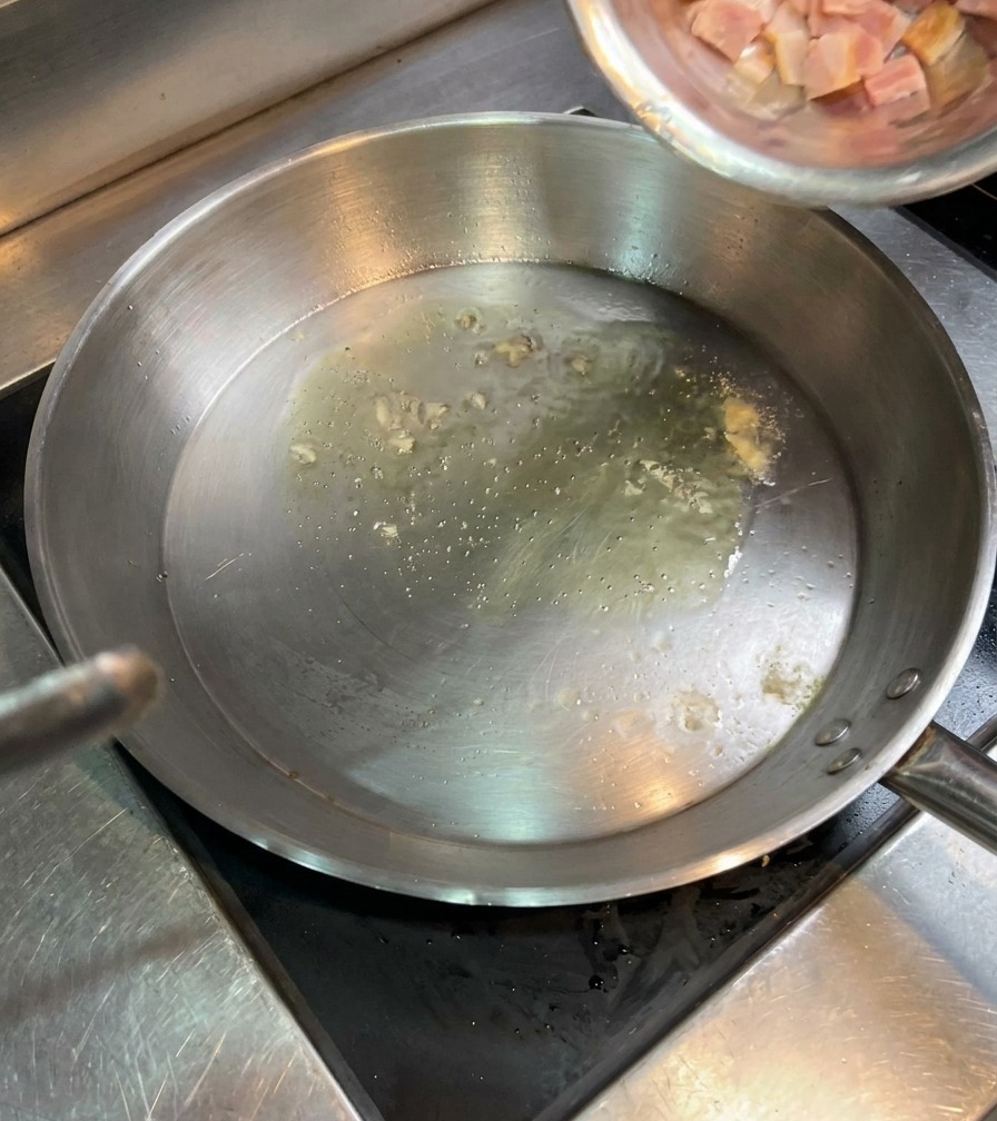 Pequeños dados de beicon crudo vertiéndose desde un cuenco a la sartén con aceite caliente.