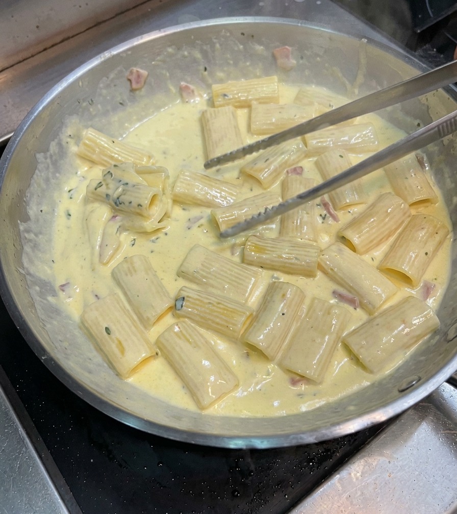 Pinzas de cocina mezclando la pasta para cubrirla bien con la salsa carbonara espesa.