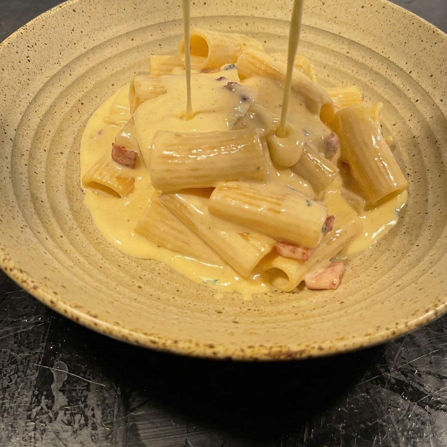 Salsa cremosa cayendo desde la sartén sobre el montón de pasta en un cuenco cerámico.
