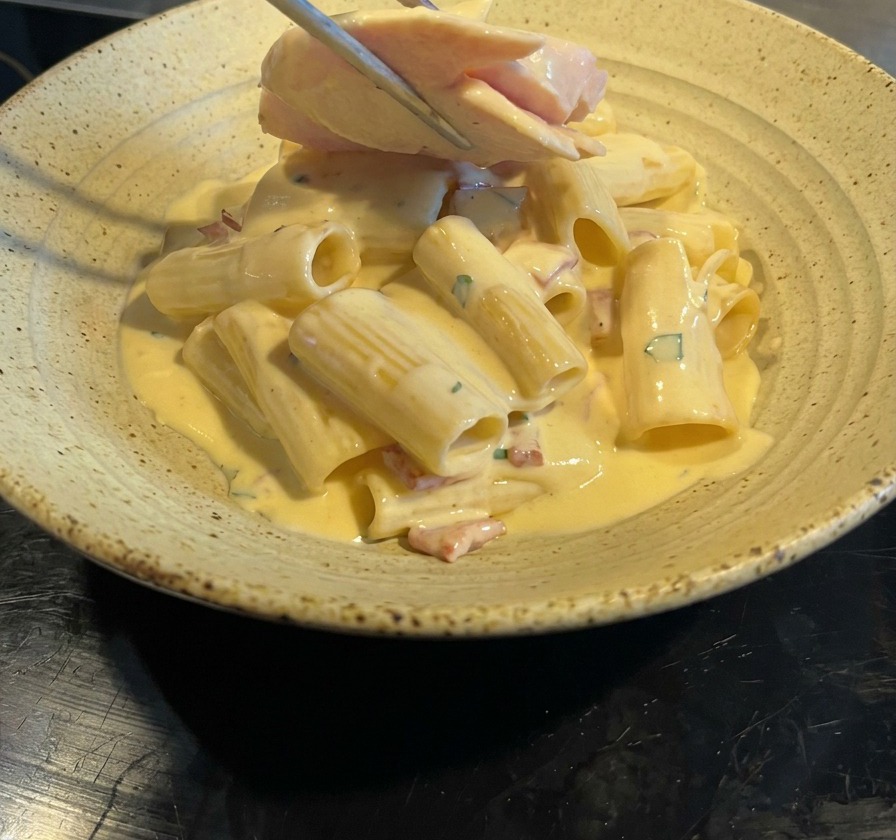 Pinzas colocando láminas de pechuga de pollo sobre los rigatoni a la carbonara.
