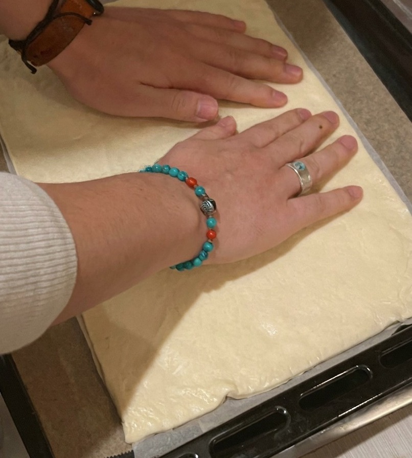 Una persona colocando una base de pizza rectangular sobre una bandeja negra forrada con papel de horno.
