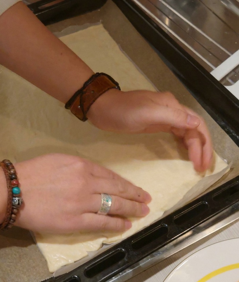 Dos manos presionando una masa de pizza rectangular para aplanarla y definir los bordes de la corteza.