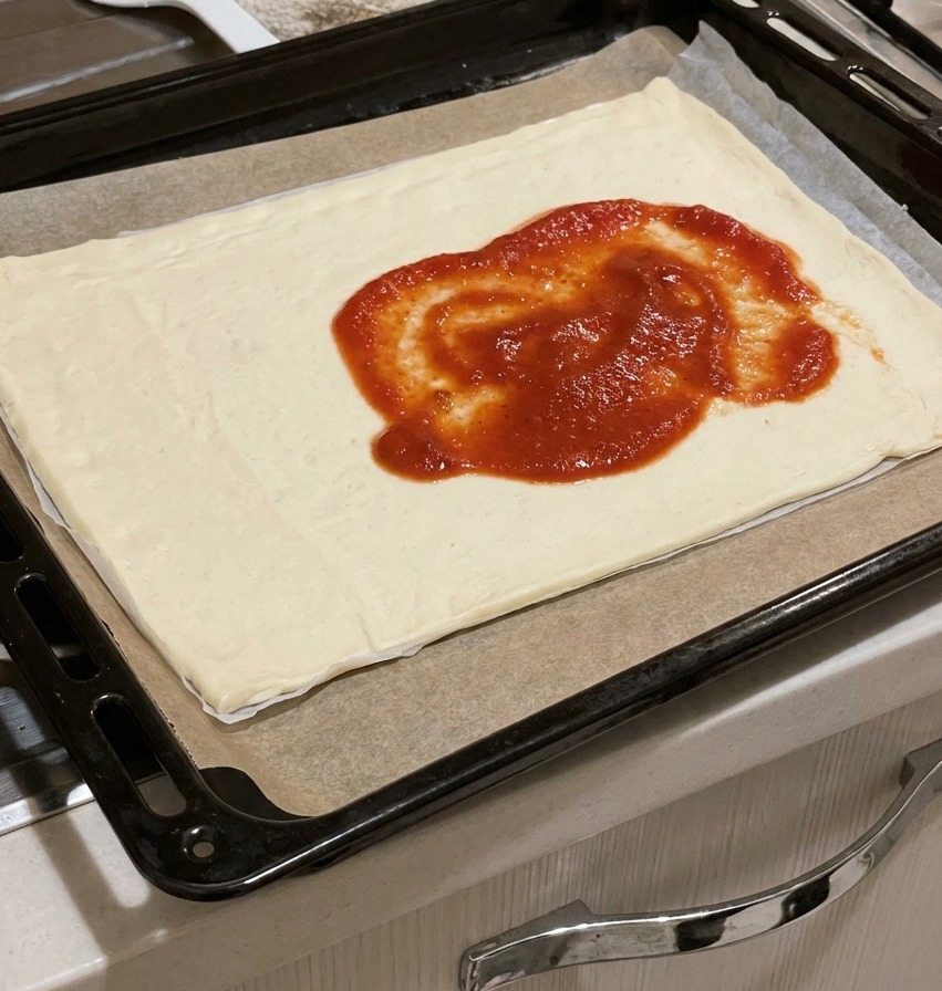 Salsa de tomate roja y espesa servida en el centro de una masa de pizza rectangular cruda sobre una bandeja.