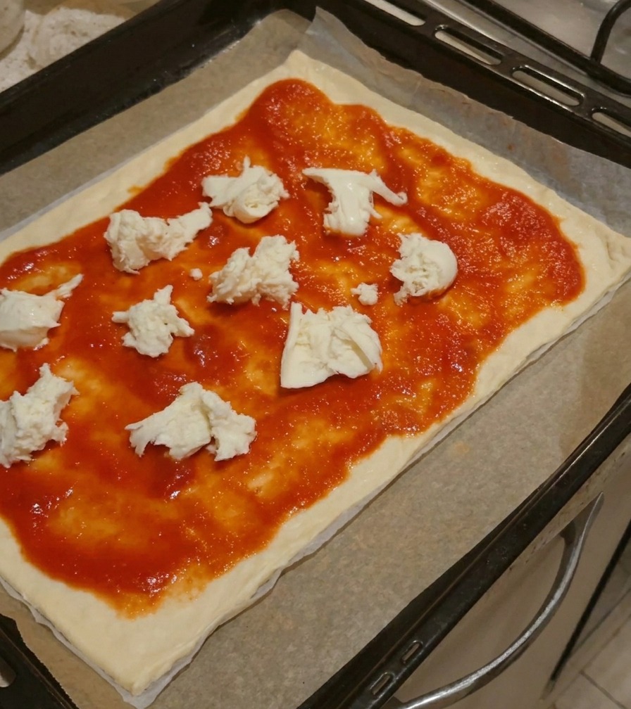 Trozos grandes de queso mozzarella blanco fresco colocados sobre la salsa de tomate en una base de pizza.
