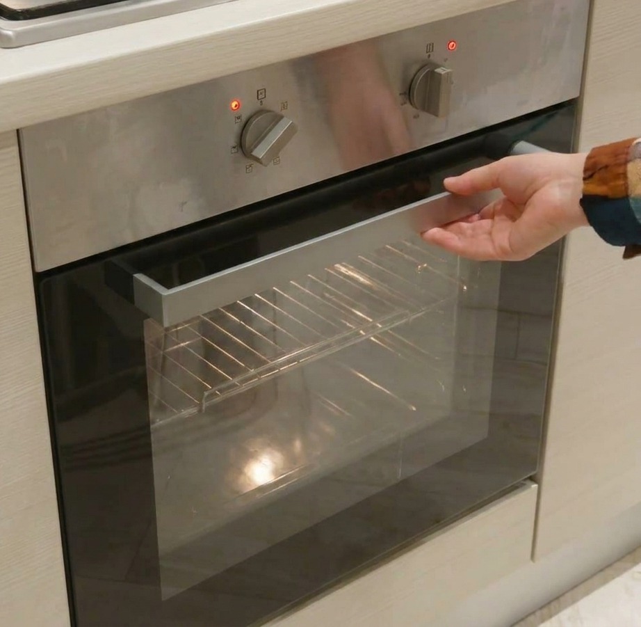 Primer plano de una mano ajustando los diales mecánicos plateados de un panel de control de horno de acero inoxidable.