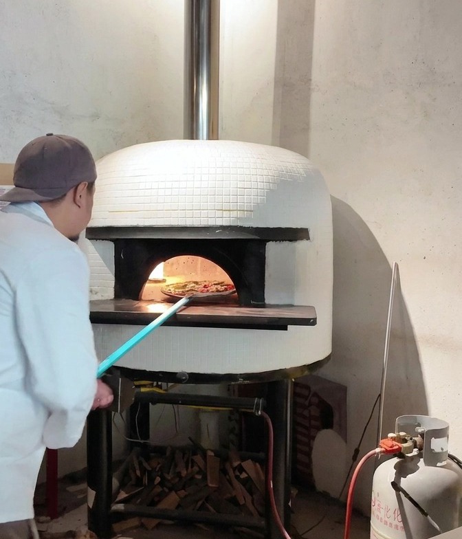 Una pizza deslizándose desde una pala de mango largo hacia el interior de un horno de leña encendido.