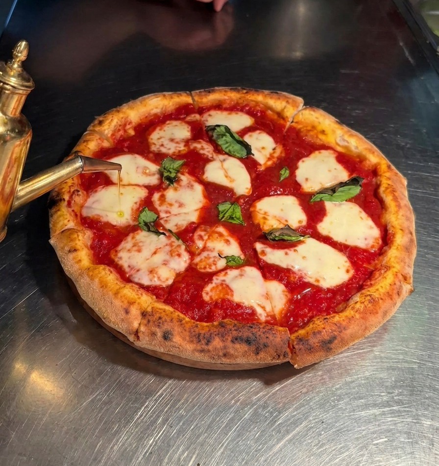 Aceite de oliva virgen extra cayendo desde un dispensador sobre una pizza Margherita cortada.