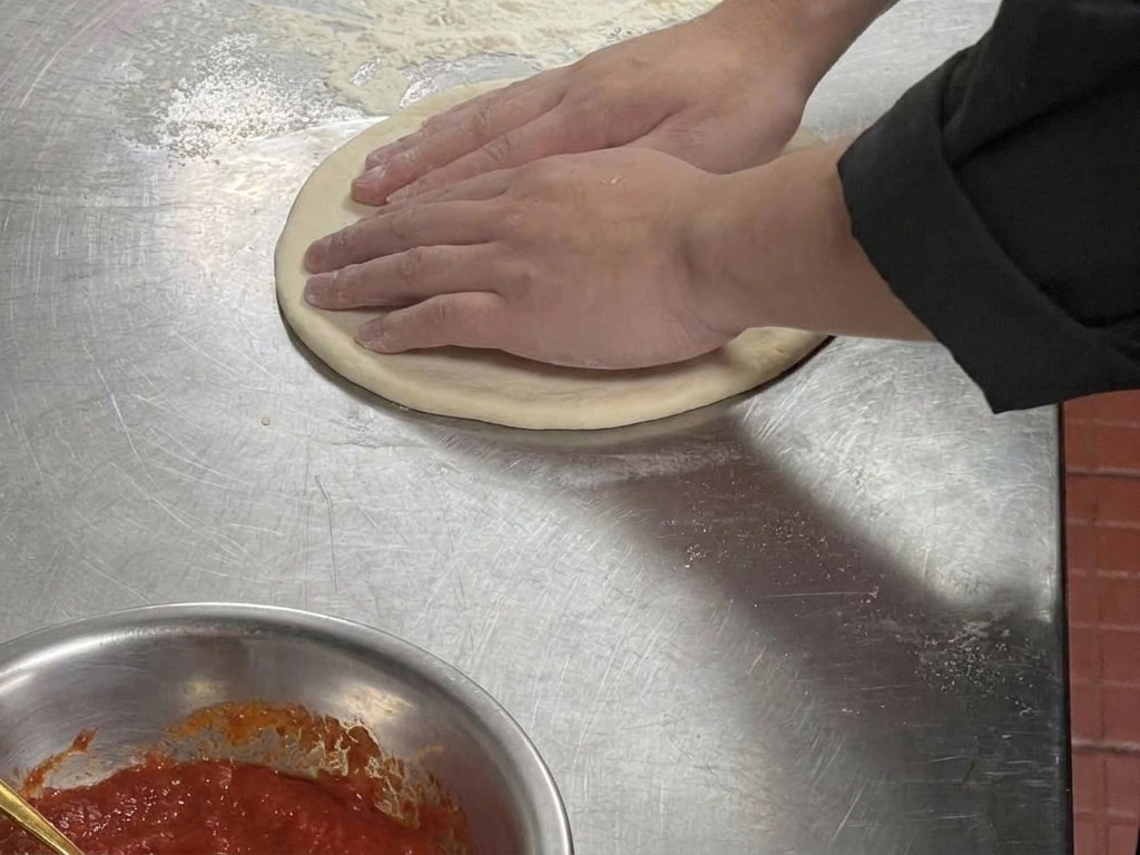 Primer plano de unas manos presionando un círculo de masa para crear un borde exterior elevado.