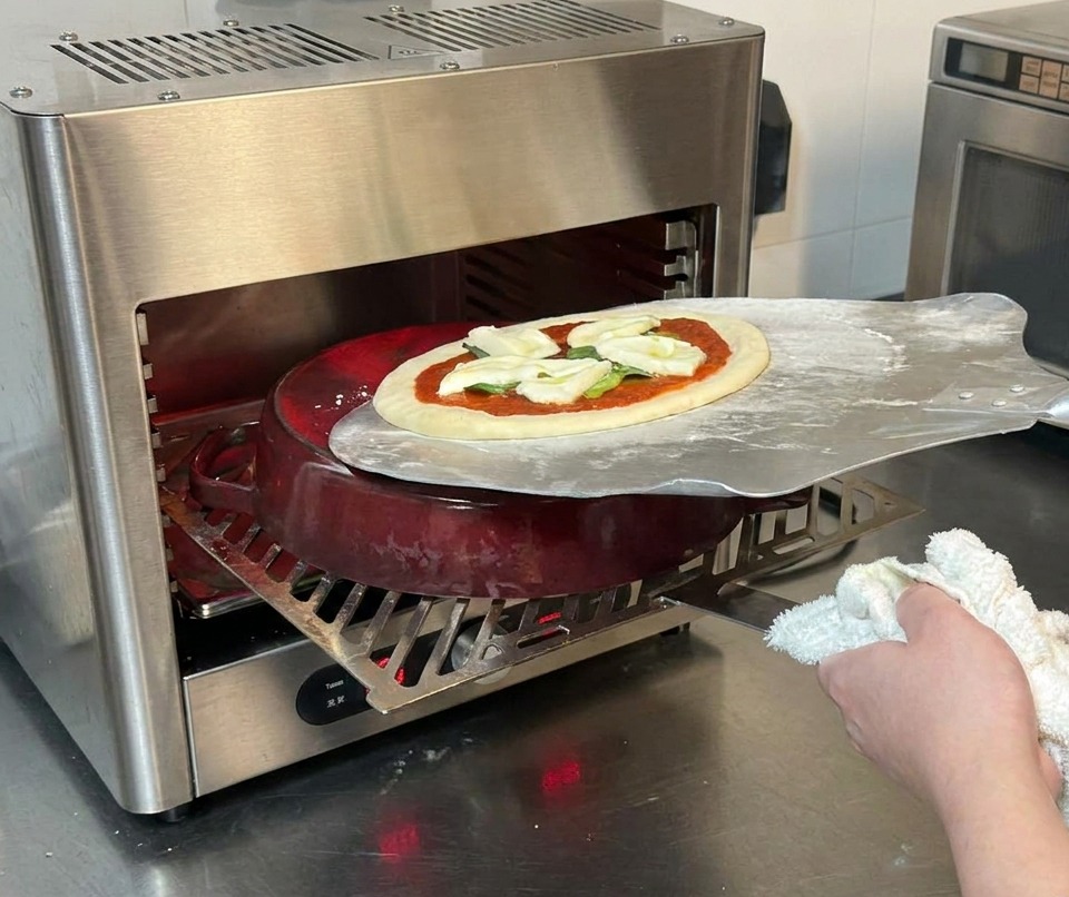 Una pala de metal deslizando una pizza cruda sobre una olla de hierro fundido dentro de un horno a alta temperatura.