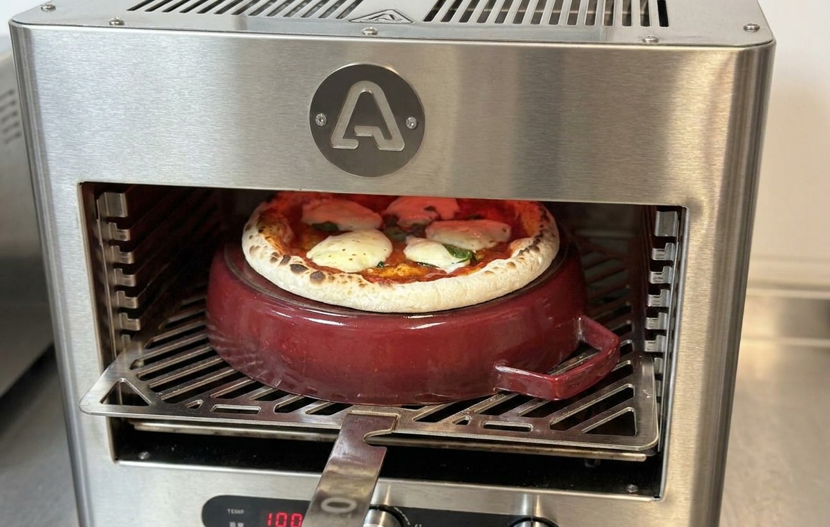 Pala de metal insertada en el horno para girar una pizza que está casi lista sobre la olla de hierro.