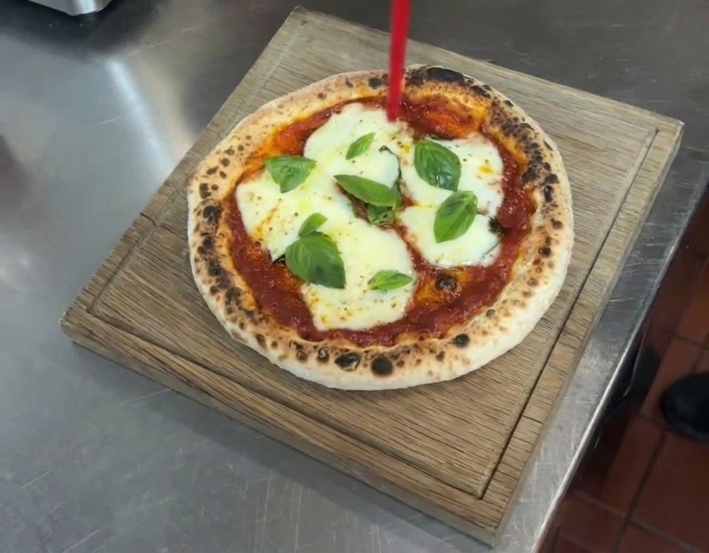 Chorro de aceite de oliva virgen extra cayendo sobre una pizza Margherita terminada en una tabla de madera.