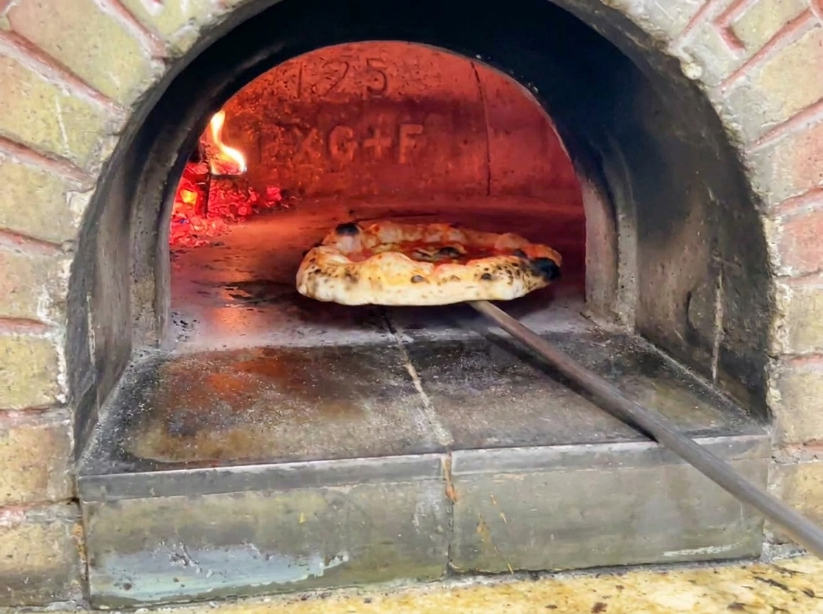 La pizza terminada saliendo del horno mostrando una masa dorada con manchas oscuras tostadas de leopardo.