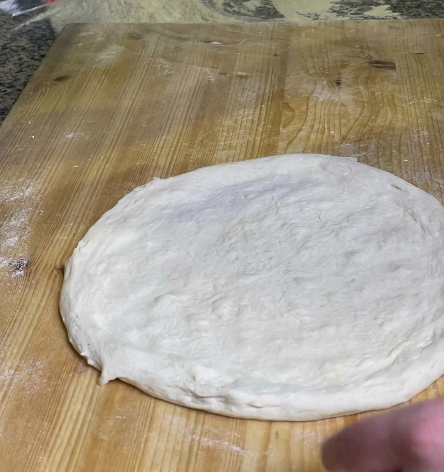 Un chef extendiendo una capa de salsa de tomate roja vibrante sobre el centro de una masa de pizza cruda en una tabla de madera