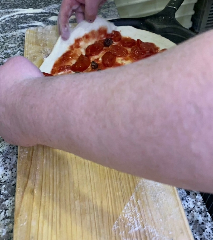 El chef deslizando una pizza cruda con sus ingredientes sobre una pala de metal negra desde un banco de trabajo de madera.