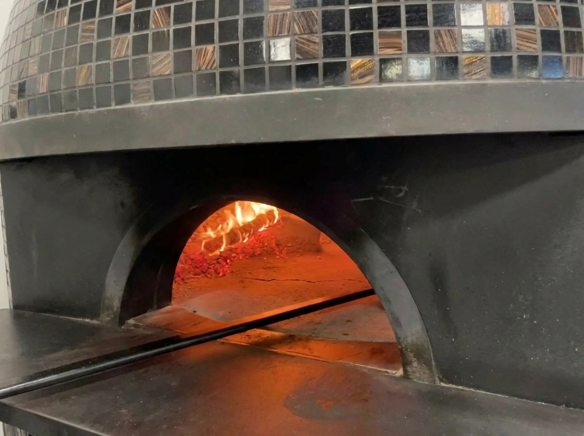 Vista del interior de un horno de pizza tradicional con llamas y una pizza cocinándose en su interior