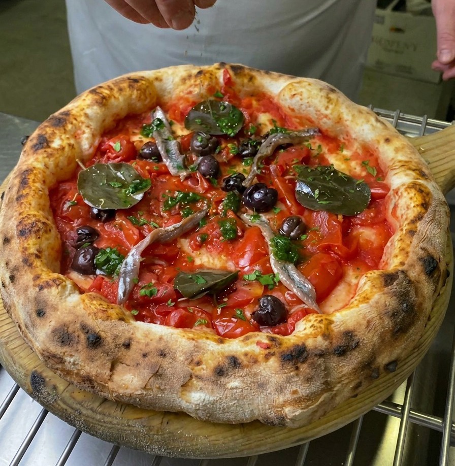 Una mano esparciendo albahaca verde fresca sobre el centro de una pizza Marinara horneada.
