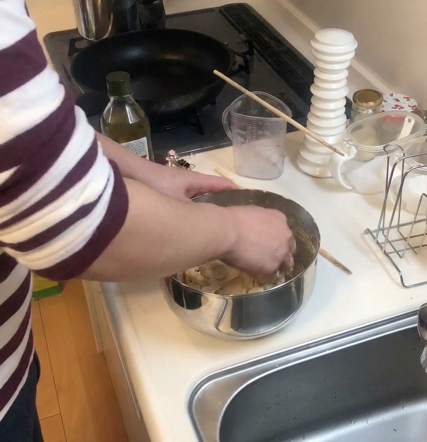 Manos amasando masa de pizza dentro de un bol de acero inoxidable sobre una encimera blanca.