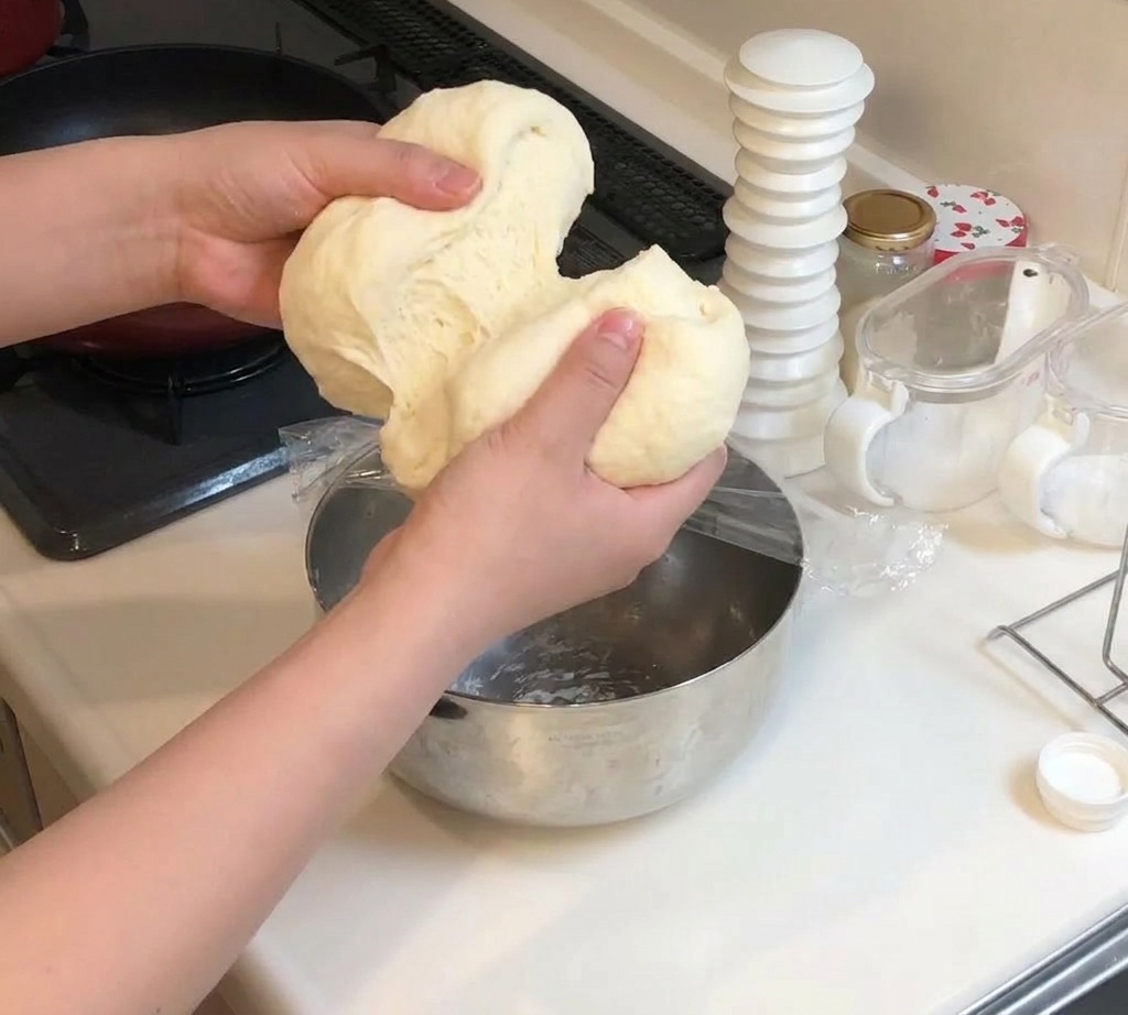 Dos manos separando un trozo grande de masa de pizza suave y elástica en dos secciones iguales.