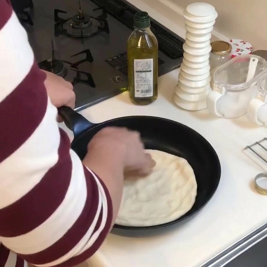 Persona usando las manos para presionar y aplanar un círculo de masa de pizza en una sartén negra.