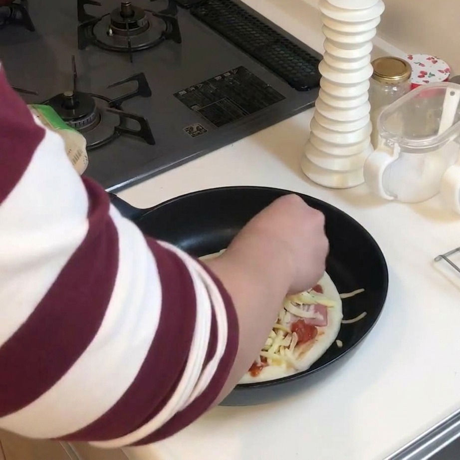 Una mano esparciendo una capa generosa de queso rallado amarillo y blanco sobre una pizza completa en la sartén.