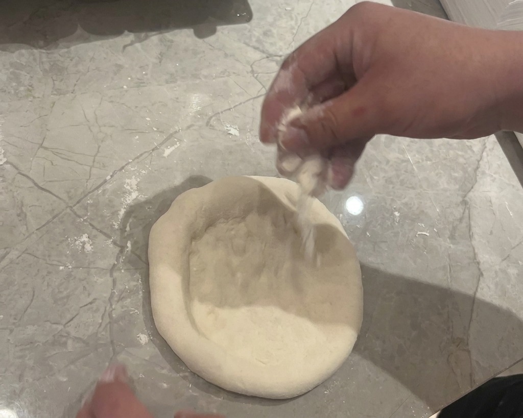 Manos presionando y aplanando una bola de masa sobre una encimera de mármol con harina blanca.