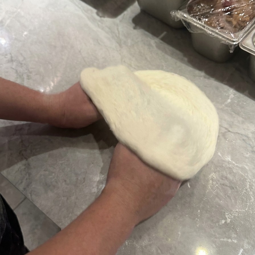 Dos manos levantando y girando la masa de pizza para darle forma circular con un borde exterior definido.