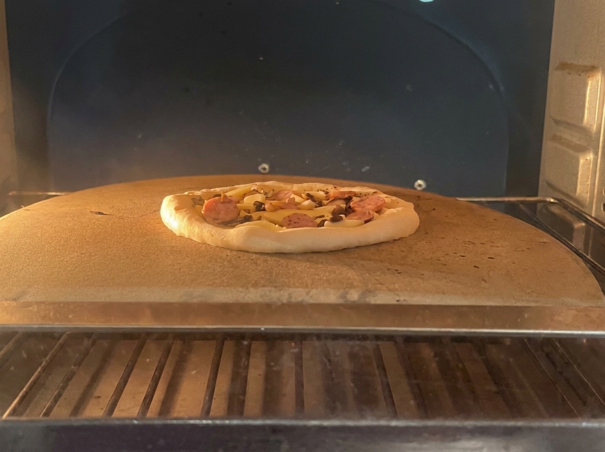 Una pizza con pepperoni y champiñones sobre una piedra de horneado dentro de un horno caliente.
