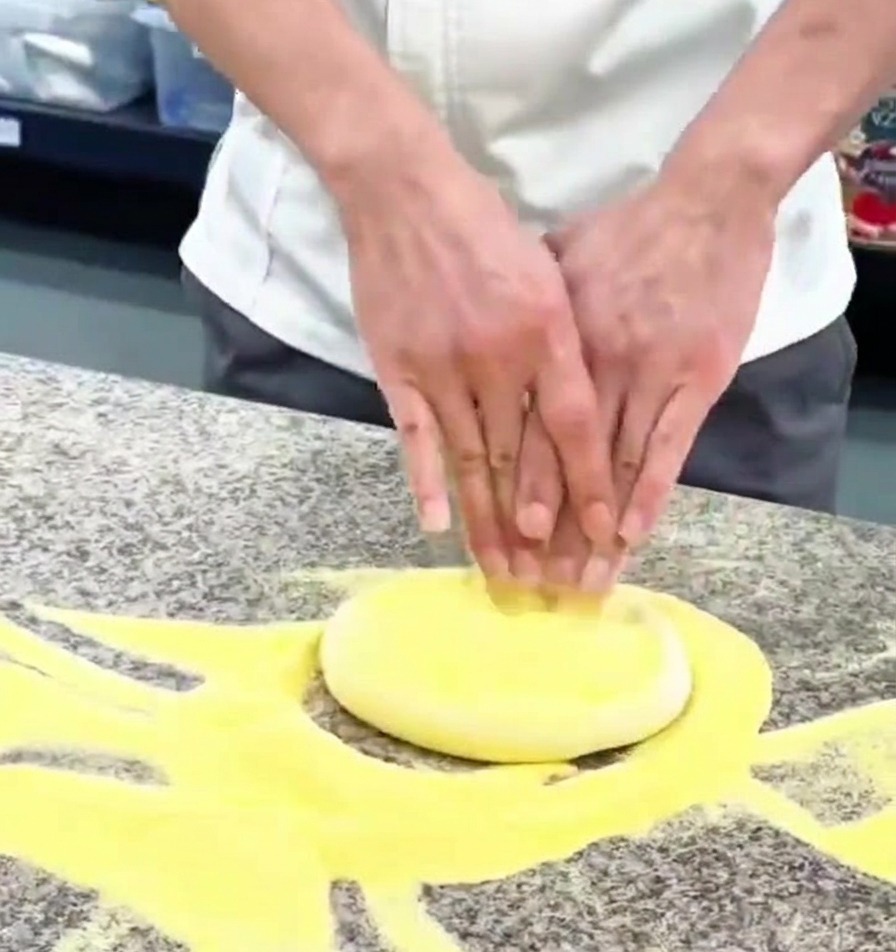 Primer plano de unas manos presionando una bola de masa de pizza sobre una encimera de granito con harina.