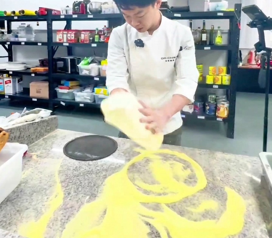 Un cocinero estirando verticalmente una base de pizza en una cocina profesional.