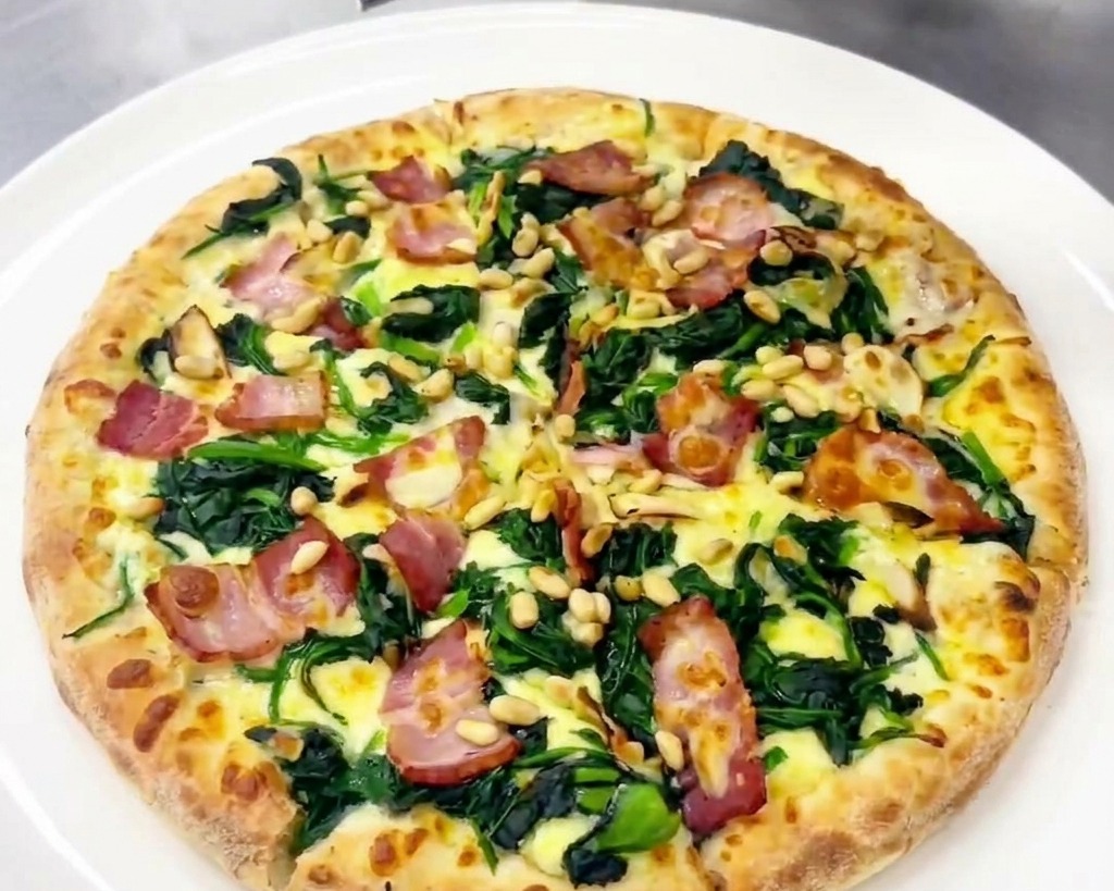 Una persona usando un rallador para añadir lascas de queso curado a una pizza cocinada.