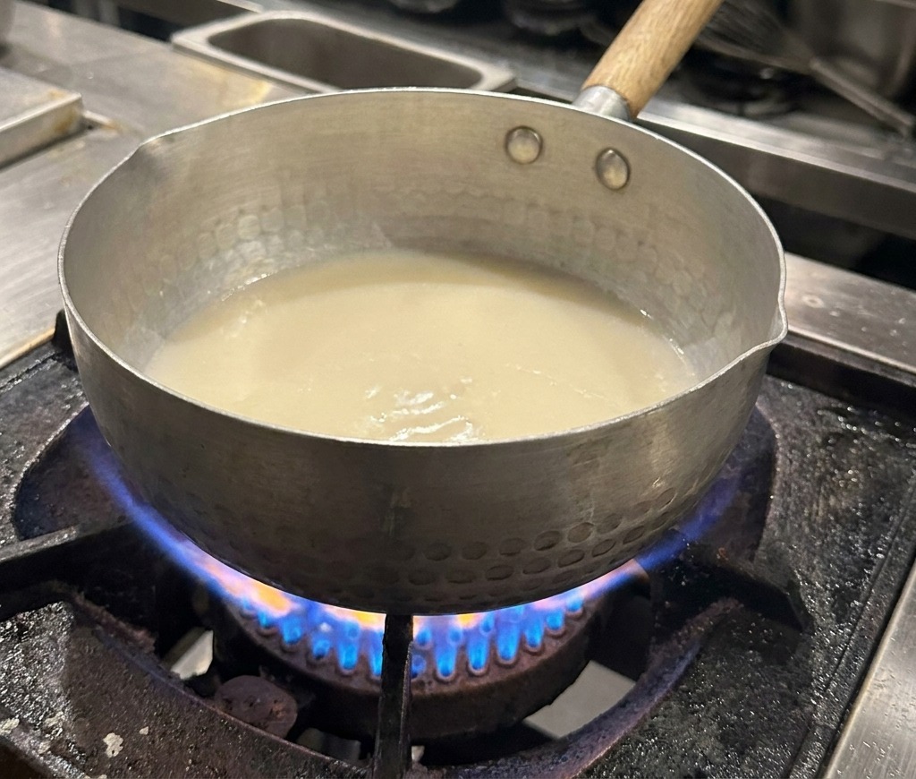 Primer plano de una olla con caldo blanco y pequeñas gotas de aceite brillantes en la superficie.