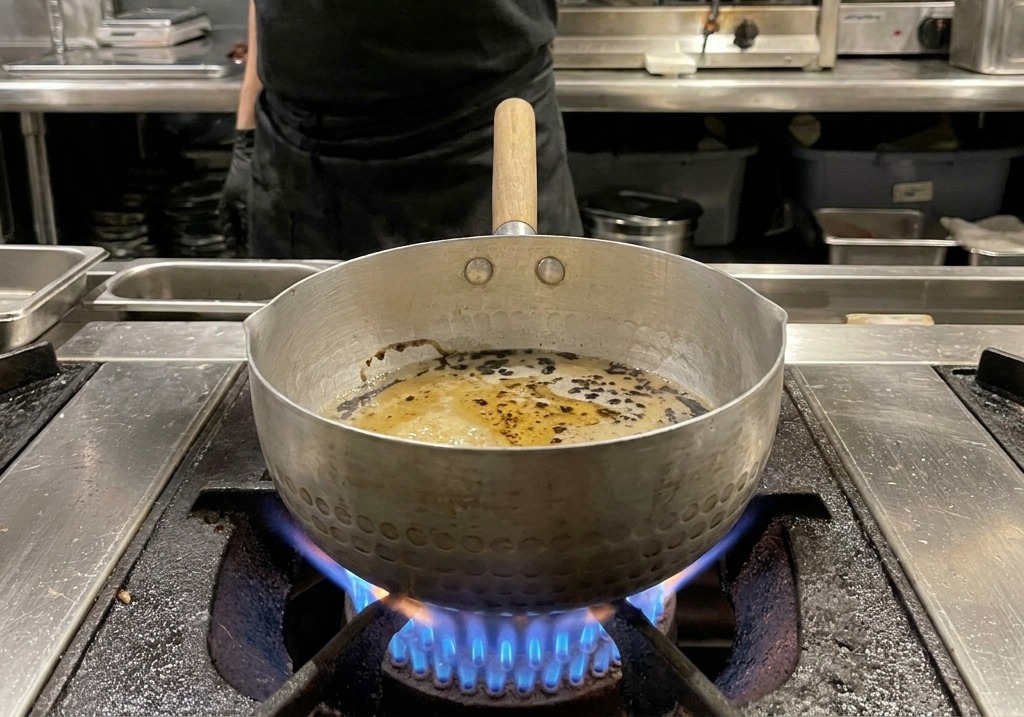 Gotas de aceite negro intenso flotando sobre la salsa marrón claro en una olla de metal.