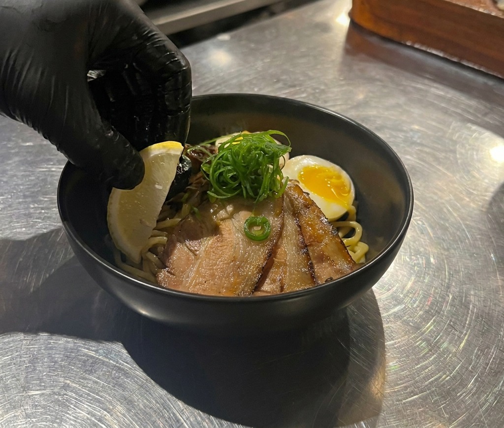 Una mano colocando una rodaja de limón amarillo en un bol de fideos japoneses.