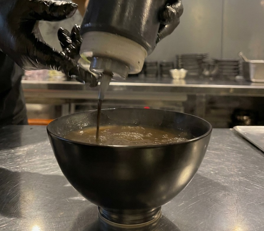Aceite de ajo negro cayendo sobre el caldo para mojar, creando círculos oscuros.