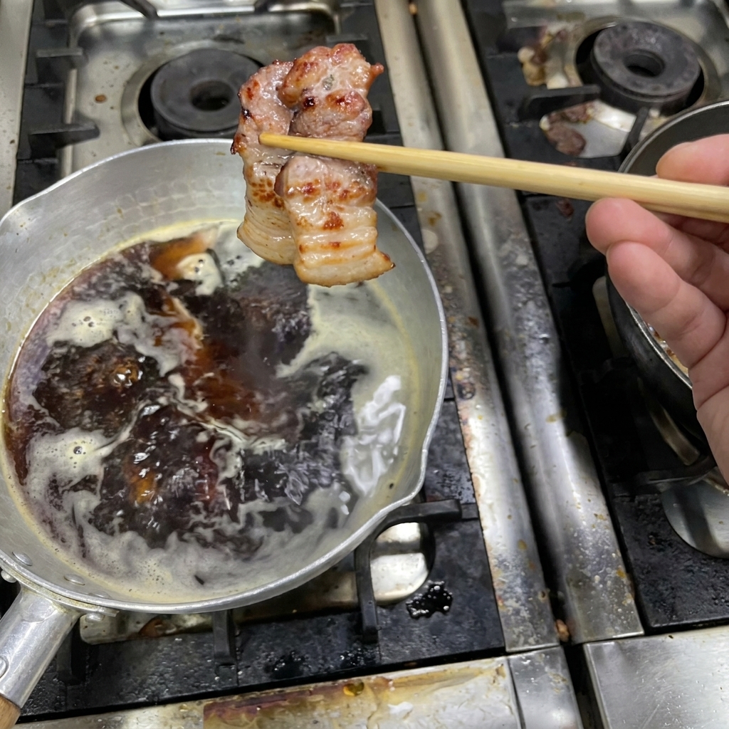 Una pieza de panceta dorada sostenida con palillos sobre una olla con salsa oscura hirviendo a fuego lento.