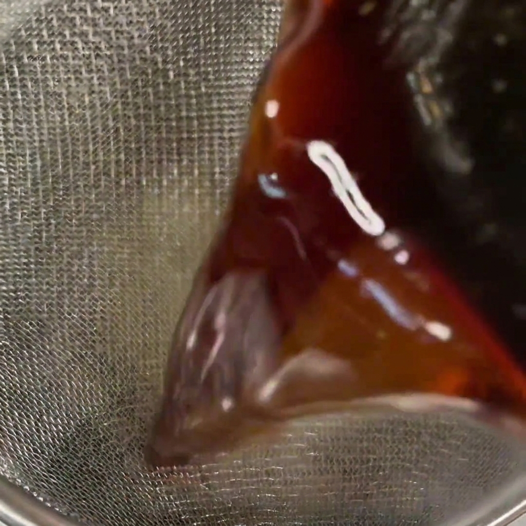 Primer plano de una salsa oscura y translúcida vertiéndose a través de un colador de malla fina.
