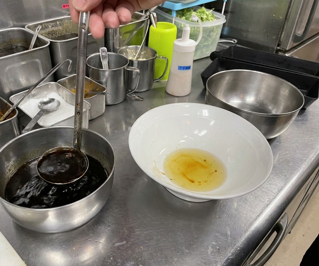 Salsa de soja oscura vertiéndose en un bol que ya contiene una capa de aceite dorado.