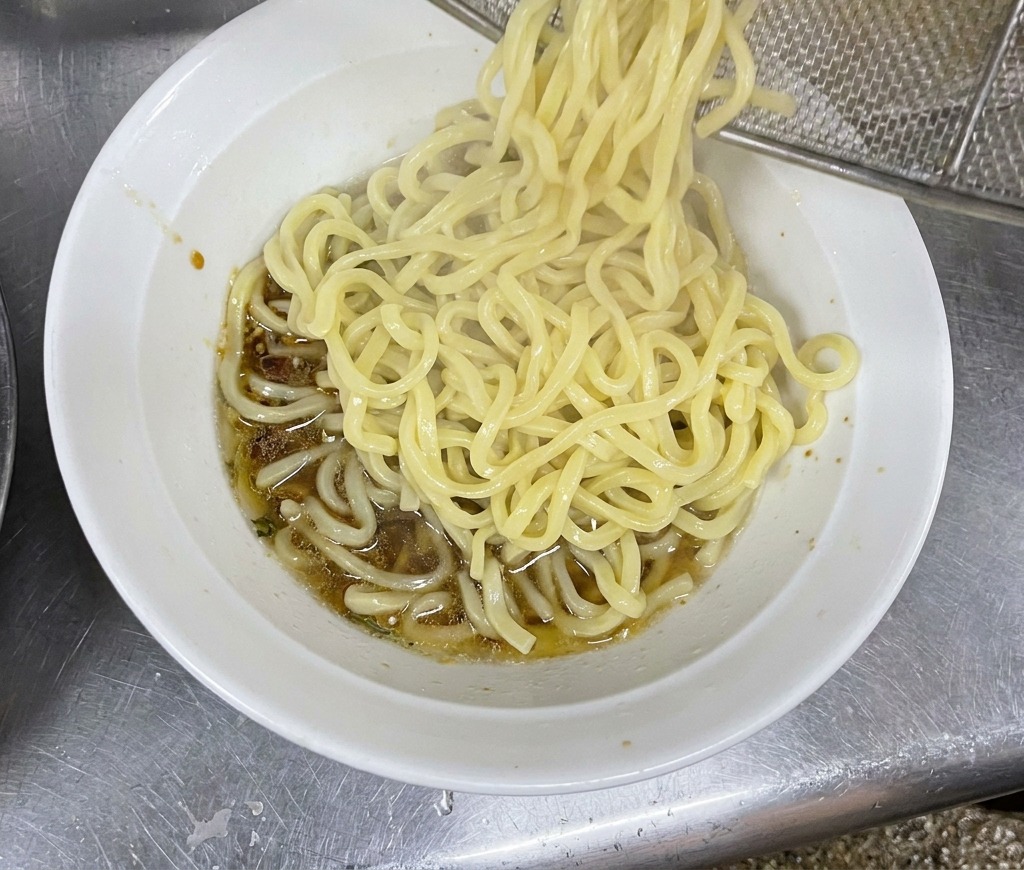 Un fajo de fideos gruesos y humeantes cayendo desde un colador de red a un bol preparado.