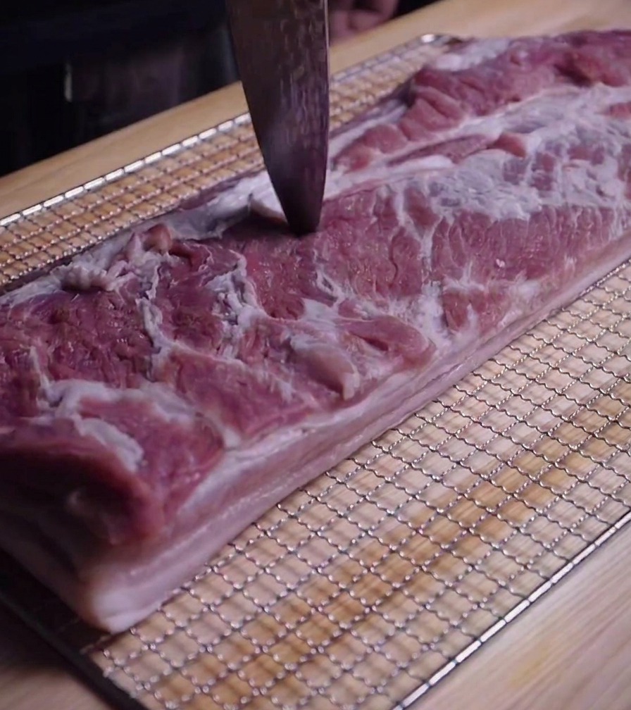 Primer plano de la punta de un cuchillo perforando pequeños agujeros en la carne de la panceta cruda.