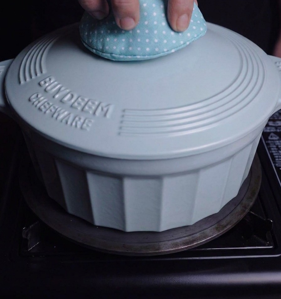 Una persona usando una manopla de cocina para tapar la olla esmaltada sobre el fuego.