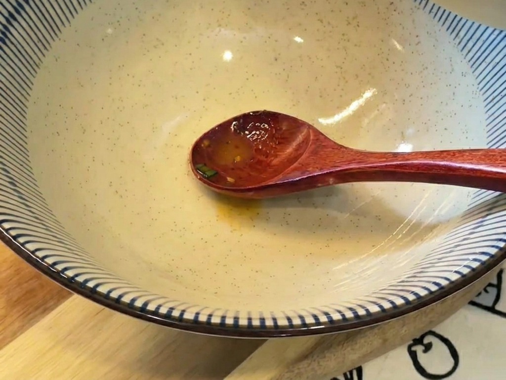 Caldo cremoso de color naranja vertiéndose de un tazón pequeño a un bol de cerámica grande con rayas azules y blancas.